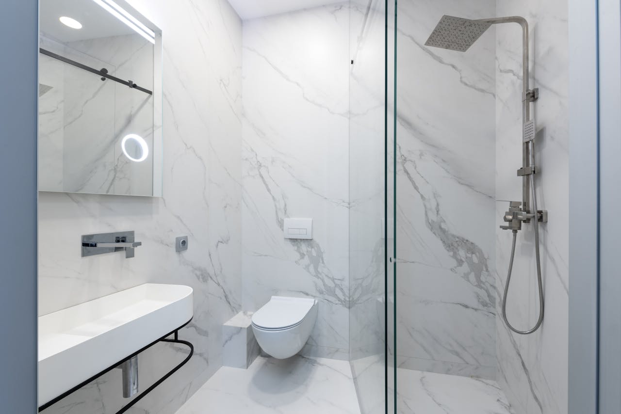 Elegant white marble bathroom featuring a sleek shower, toilet, and sink.