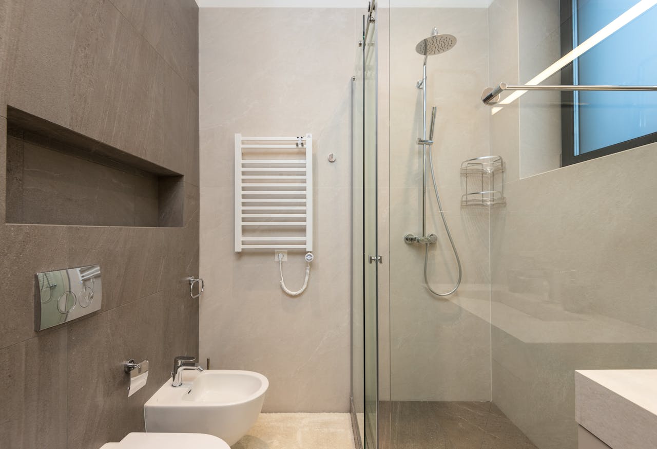 Interior of modern bathroom with glass shower cabin in front of white ceramic toilet bowl and bidet